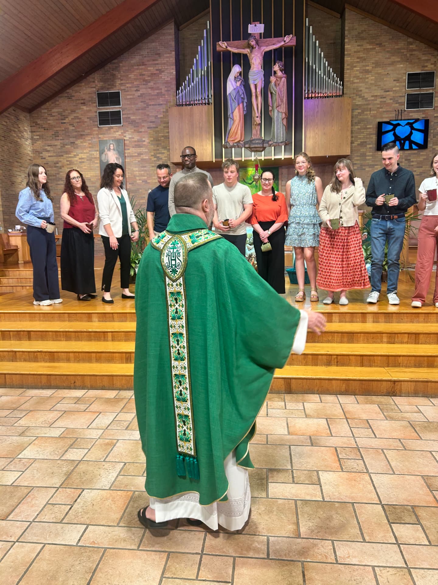 Fr. Jim in green vestments greeting parishioners holding mugs in the sanctuary