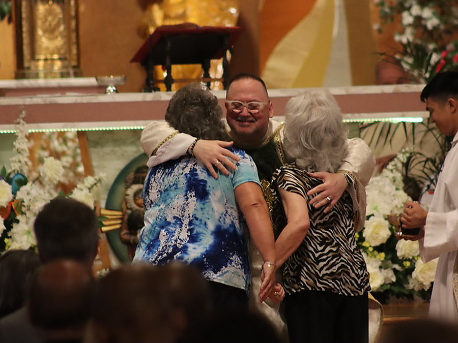 Fr. Jim embracing two parishioners at the front of the church, an altar server beside them