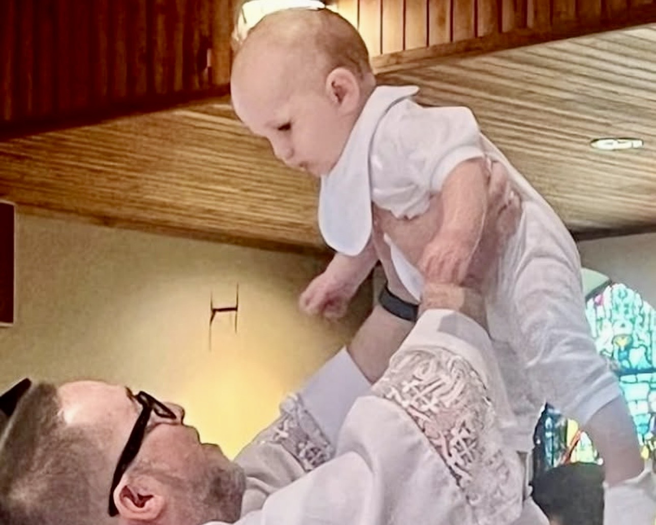 A priest in white vestments lifts an infant during a Baptism at St. Joseph