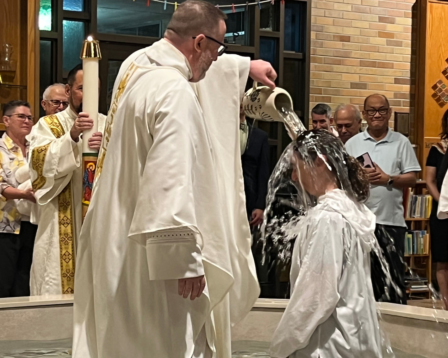 A priest pours water over an adult candidate in the baptismal font while a server holds the Paschal candle
