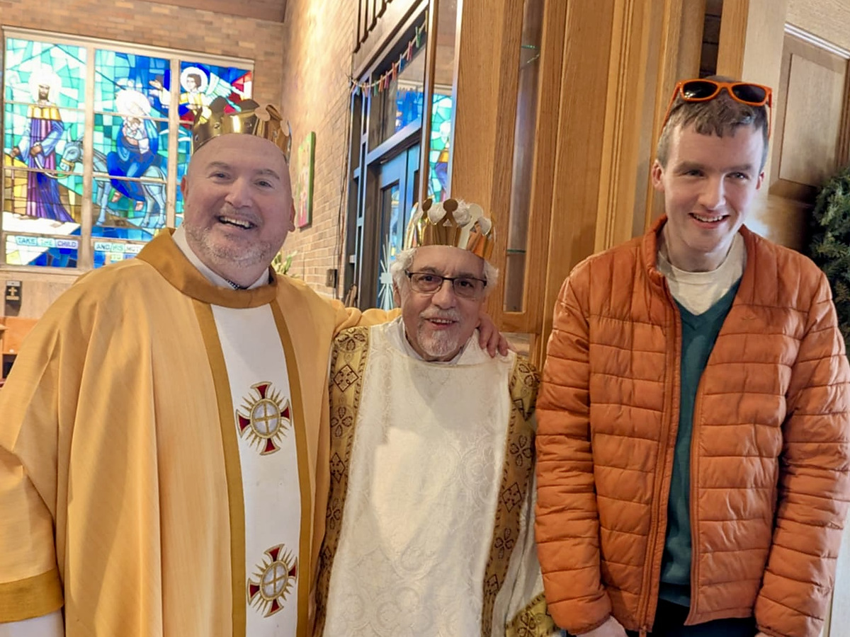 Three men wearing paper crowns inside the church, a stained glass window beside them