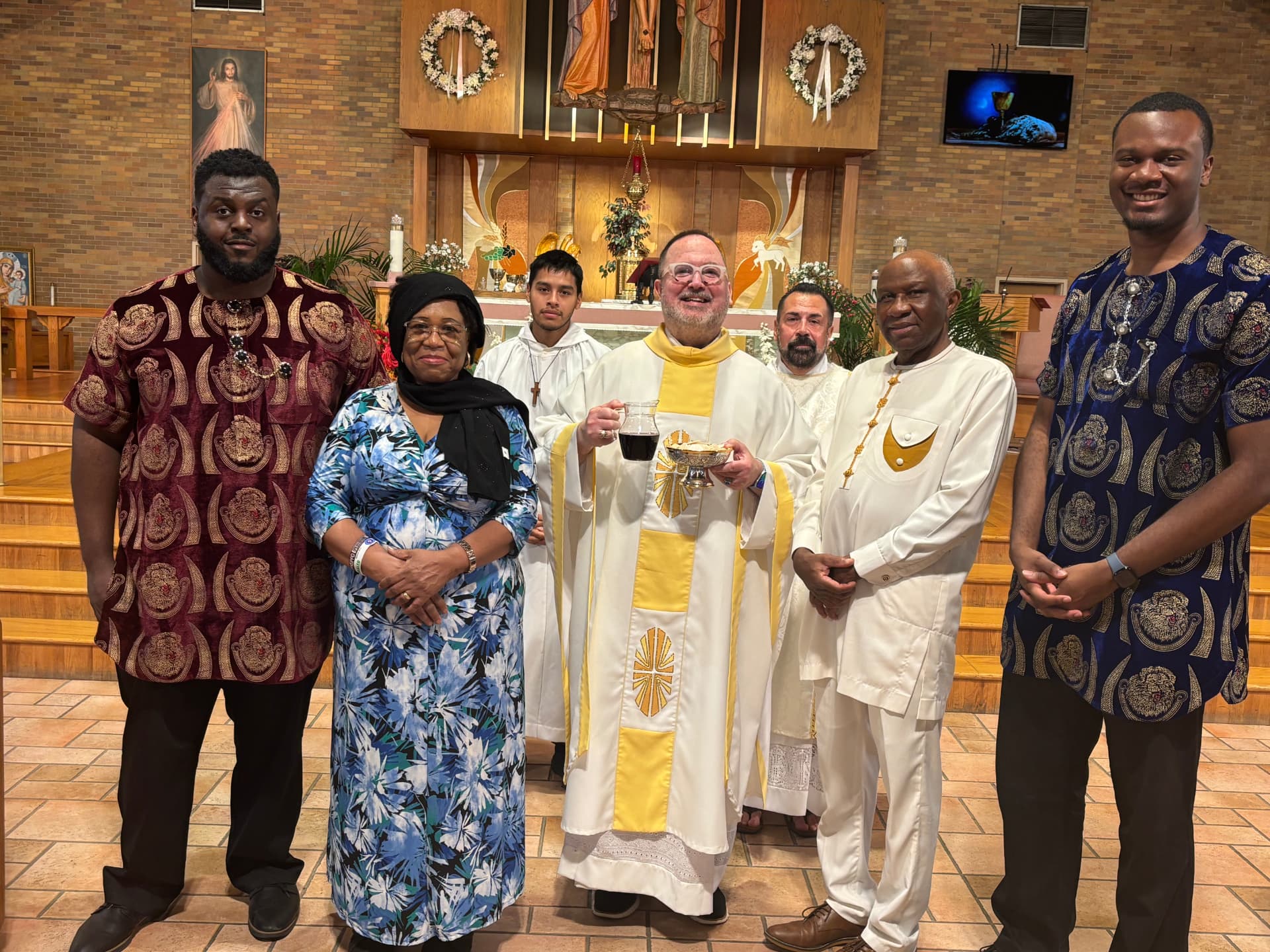 Fr. Jim holding the gifts of bread and wine with parishioners in traditional dress at the altar